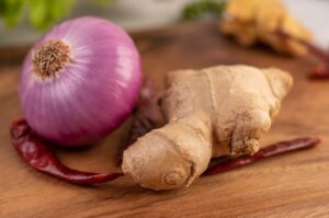 Fresh ginger, garlic cloves, and a sliced onion on a cutting board